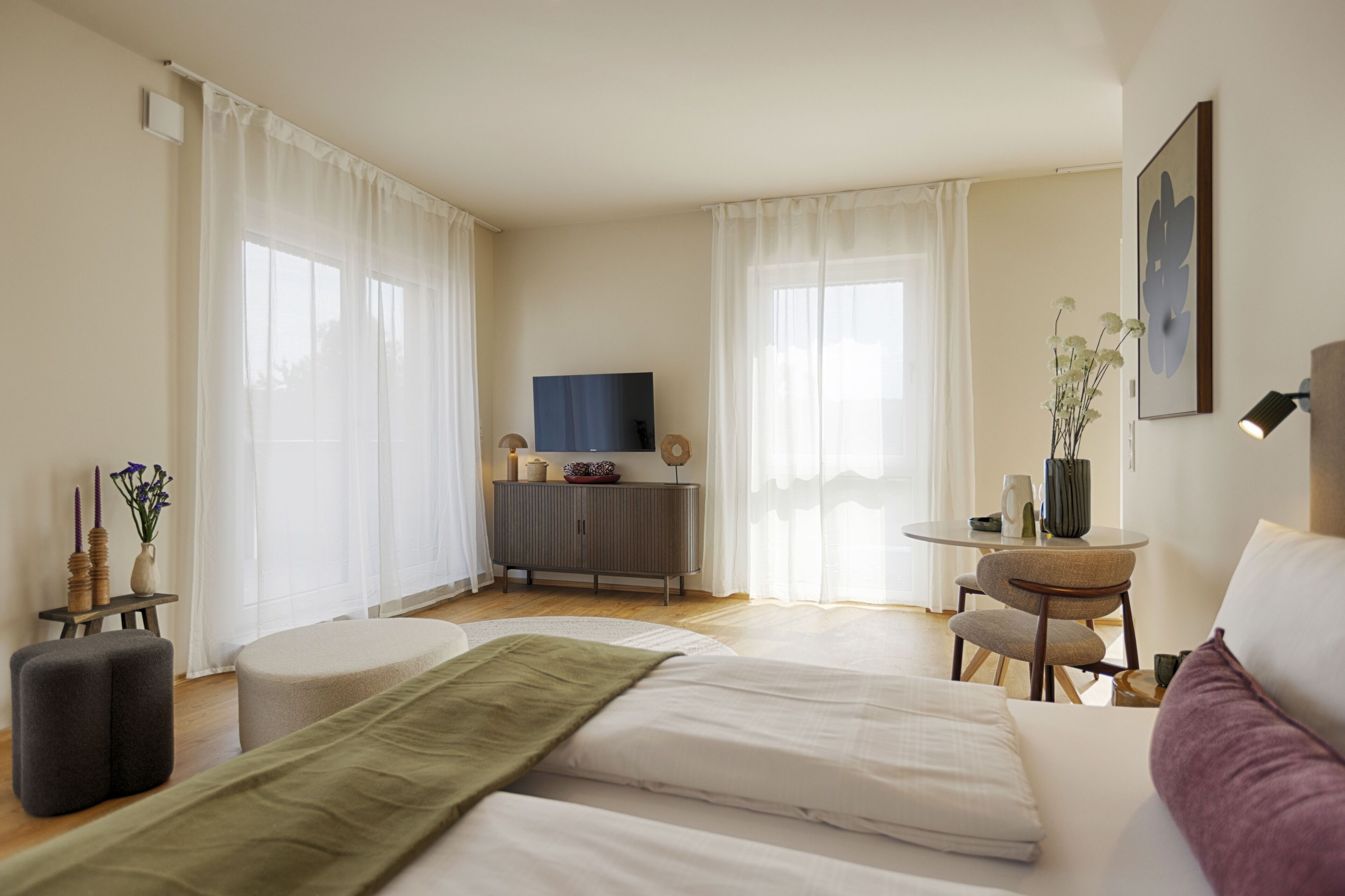 A well-lit room with a bed, a small table, a TV, and a cabinet.
