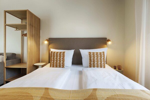 A hotel room with a double bed, two pillows, a bedside table, a lamp, and a wooden shelf unit. - homie stay am sonnenstuhl (Randersacker)