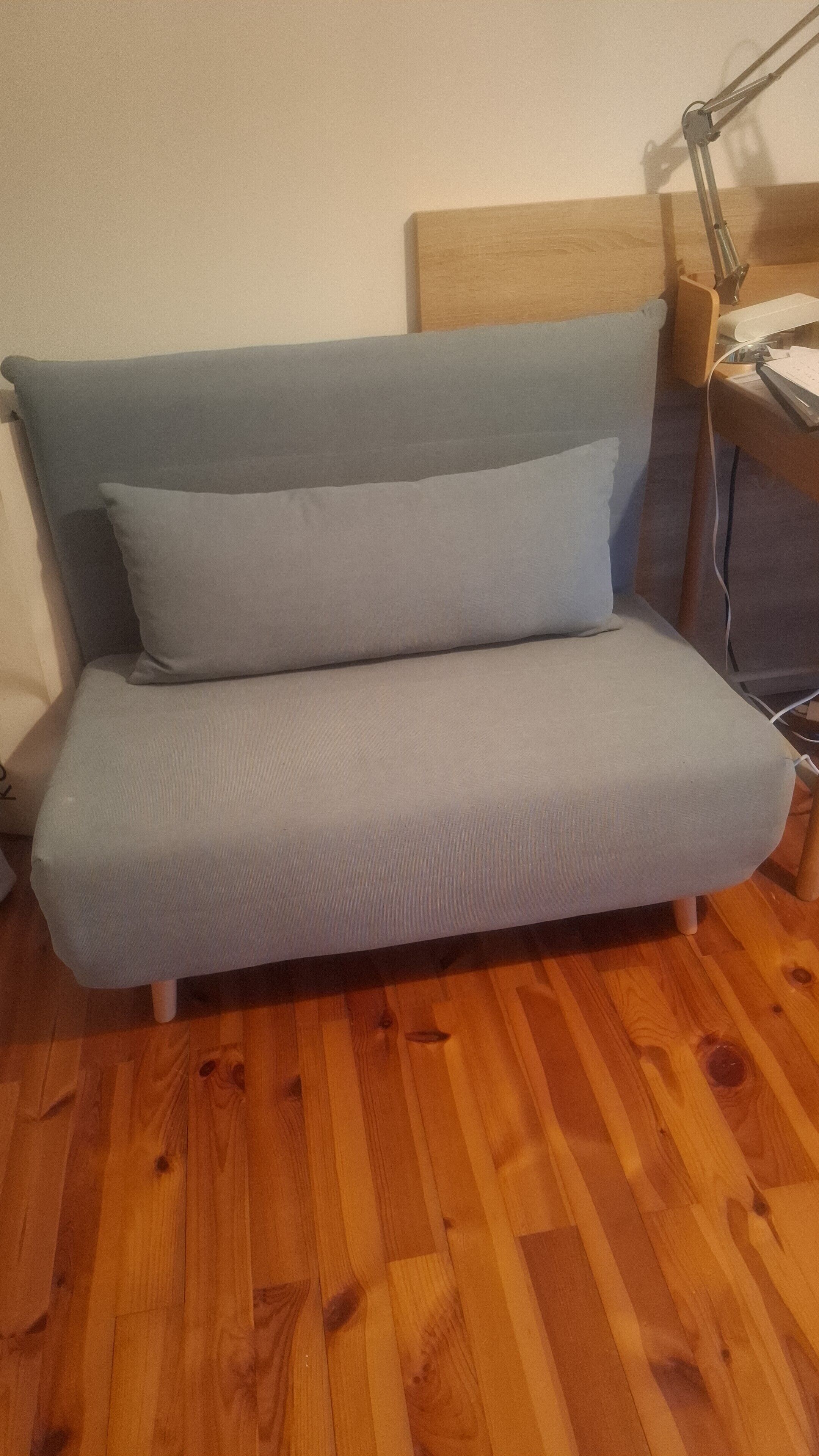 A sofa with a wooden headboard, a desk with a lamp, and a wooden floor.