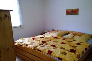 Un letto singolo con struttura in legno, coperta con motivo giallo e rosso, e un quadro appeso al muro raffigurante fiori rossi.
