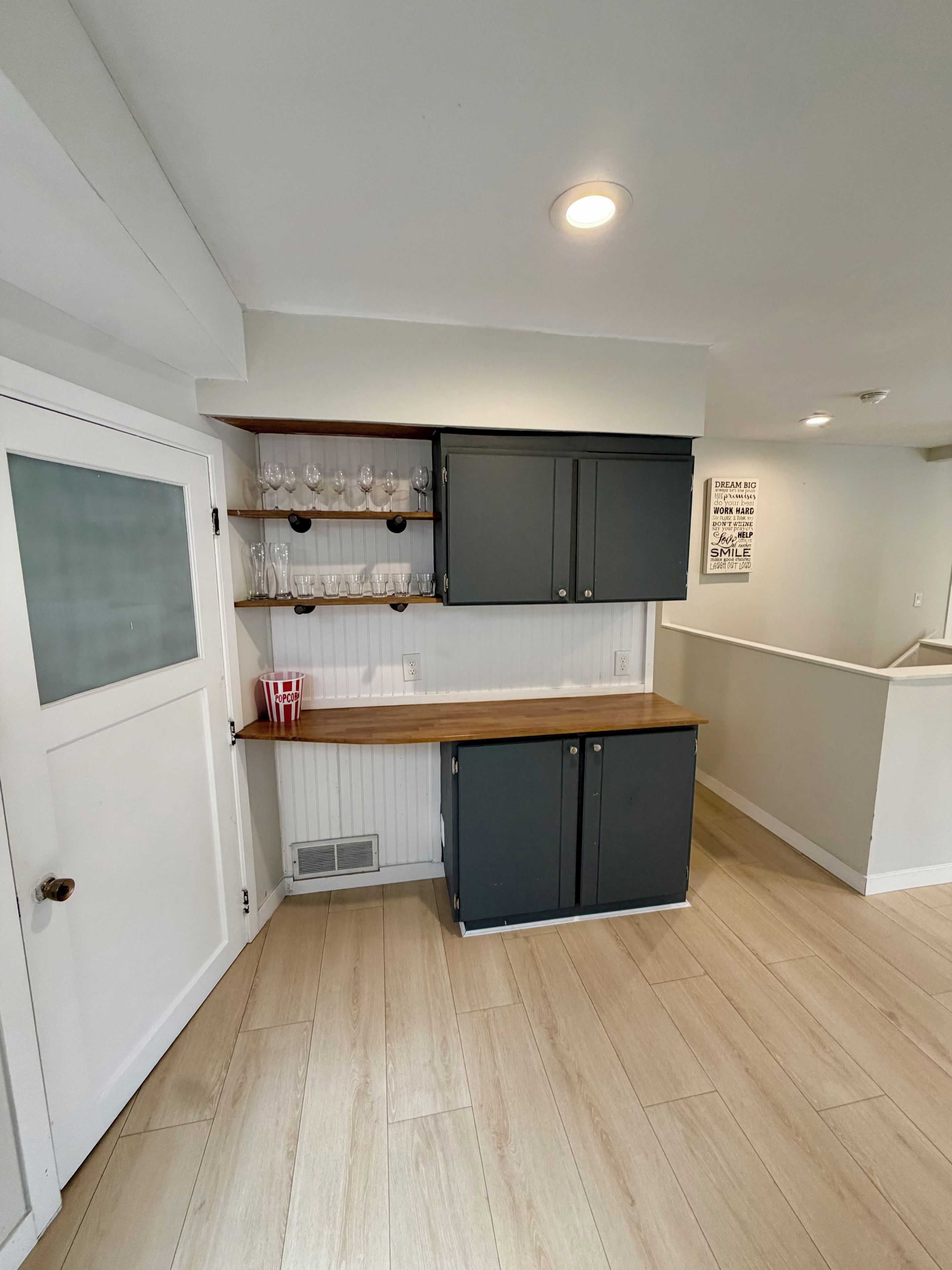 A compact kitchen with white walls, wooden flooring, and a built-in dark-colored cabinet.