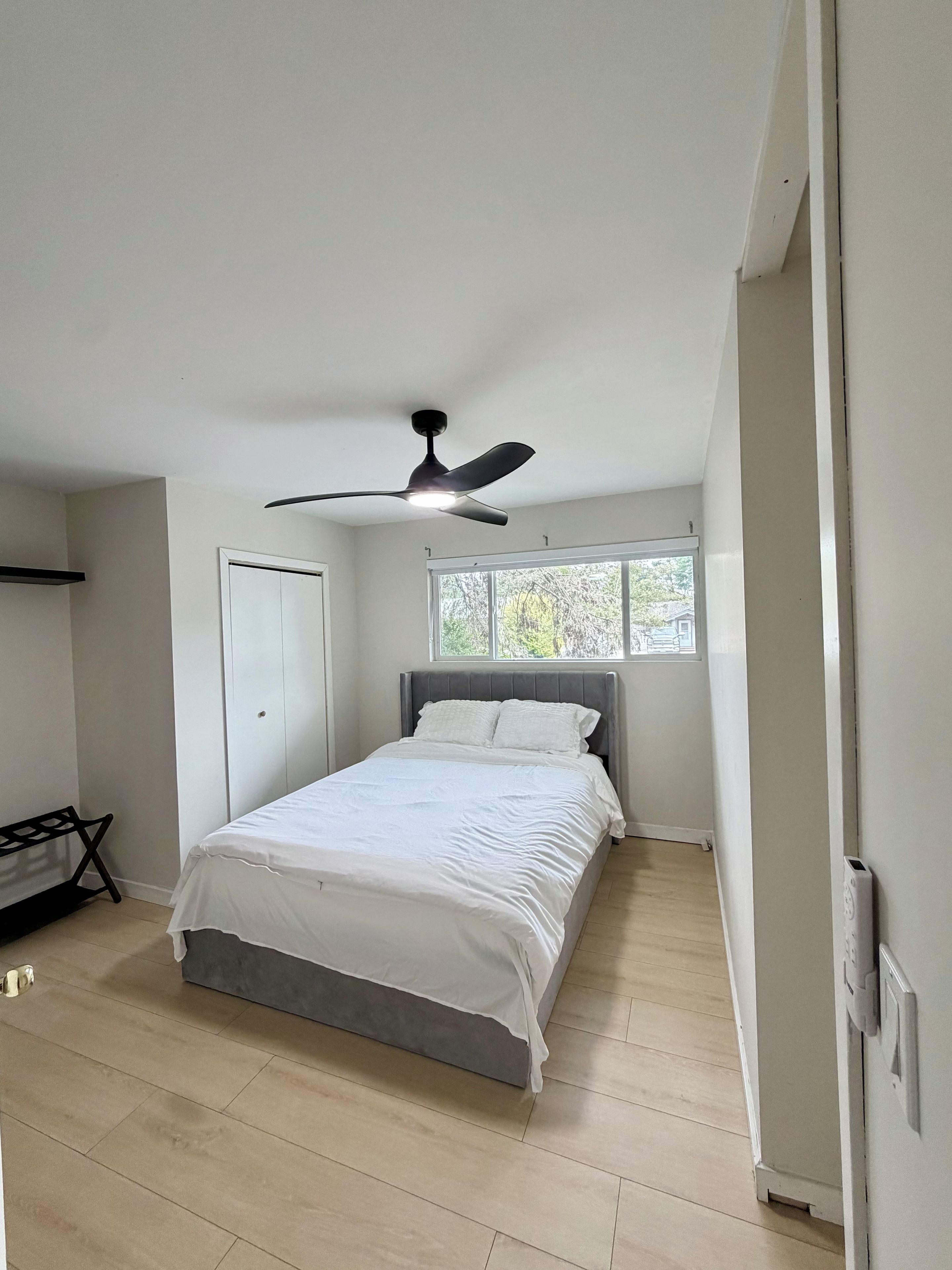 Ein Schlafzimmer mit Bett, Deckenventilator, Fenster und Tür.