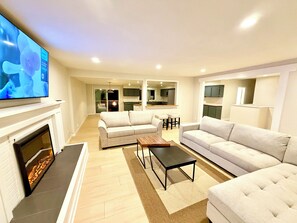 A modern living room with a fireplace, sofas, a coffee table, and a TV. - Ultimate Oasis-Waterpark, FIFA!, Games & Huge Yard (Langley Township)