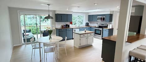 A modern kitchen with a central island, a dining area with a round table, and a view of a deck.