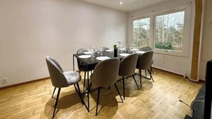 Ein Essbereich mit Tisch für vier Personen, umgeben von Stühlen, in einem Raum mit Holzboden und einem großen Fenster.