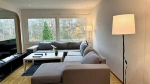 Ein modernes Wohnzimmer mit einem Ecksofa, einem Flachbildfernseher, einem Couchtisch und einer Lampe.