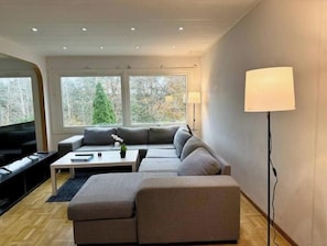Ett modernt vardagsrum med en hörnsoffa, en platt-TV, ett soffbord och en lampa.