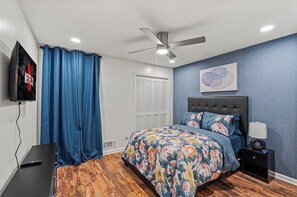 Un dormitorio con cama, ventilador de techo, televisor y mesita de noche.