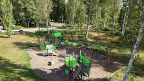 Leikkikenttä, jossa on keinut, liukumäet ja kiipeilytelineitä, ja kaiken ympärillä on puita.