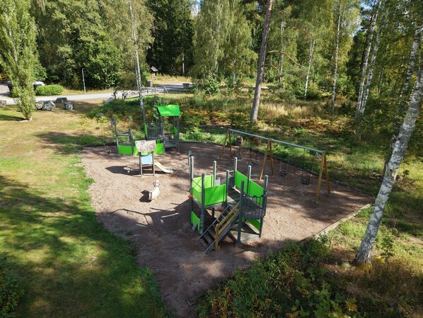 A playground with swings, slides, and climbing structures surrounded by trees.