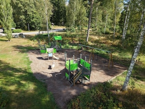 A playground with swings, slides, and climbing structures surrounded by trees. - Ekängens vandrarhem (Virserum)