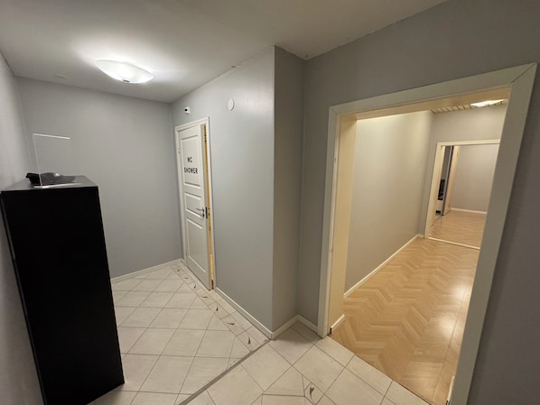 A hallway with a tiled floor, a door labeled 'WC SHOWER,' and a black object on a pedestal. - Ekängens vandrarhem (Virserum)