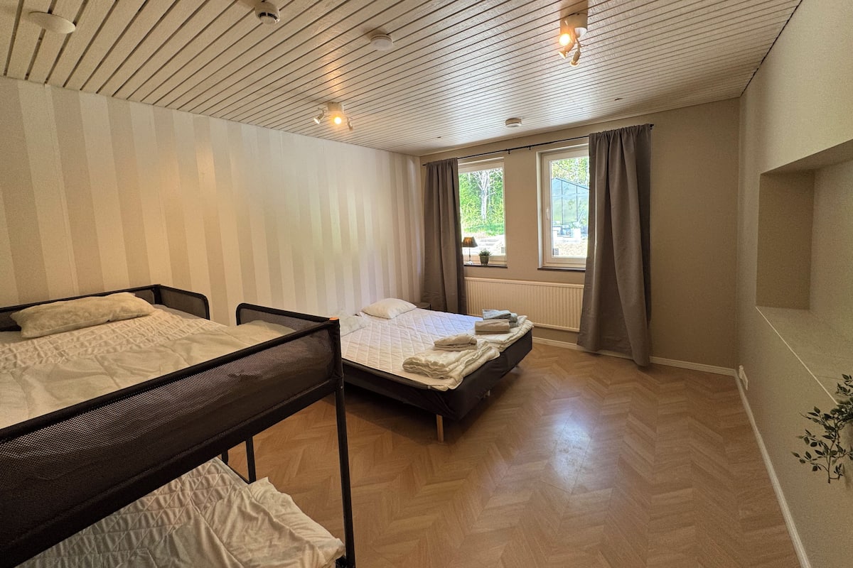 Una habitación con dos camas, una ventana con cortinas, un radiador y un techo de listones de madera.