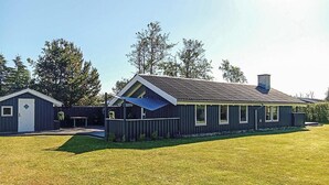 A single-story building with a sloped roof, a fenced yard, and a small adjacent shed. - Cozy home in Strandby with sauna (Strandby)