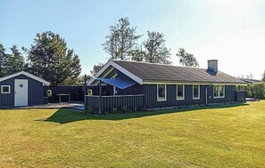 A single-story building with a sloped roof, a fenced yard, and a small adjacent shed. - Cozy home in Strandby with sauna (Strandby)