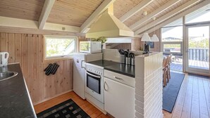 A compact kitchen with a microwave, oven, and sink, wooden walls, and a view to the outside. - Cozy home in Strandby with sauna (Strandby)
