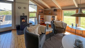 A cozy living room with a fireplace, comfortable seating, and large windows offering a view of the outdoors. - Cozy home in Strandby with sauna (Strandby)