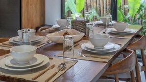 Comedor con mesa de madera dispuesta para cuatro, rodeado de lámparas colgantes de mimbre.