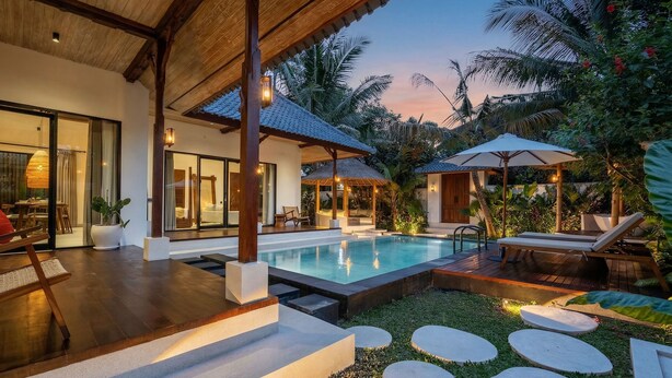 Un área de piscina moderna al aire libre con una zona de estar cubierta, una tumbona y un jardín bien cuidado.