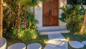 Un resort tropical con una puerta de madera, una estructura de techo de paja y un camino de hormigón que conduce a la entrada.