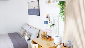 A compact bedroom with a bed, a desk, a chair, a blue sofa, and a wall-mounted shelf with plants. - Homeku Guesthouse Room 4 Cozy Stay Close to Suvarnabhumi Airport (Lat Krabang)