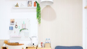 A modern room with a desk, chair, blue sofa, wooden floor, white walls, and a hanging plant. - Homeku Guesthouse Room 4 Cozy Stay Close to Suvarnabhumi Airport (Lat Krabang)