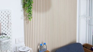 A modern living room with a wooden slat wall, a hanging plant, a white pendant light, a blue sofa, a wooden coffee table, and a kettle. - Homeku Guesthouse Room 4 Cozy Stay Close to Suvarnabhumi Airport (Lat Krabang)