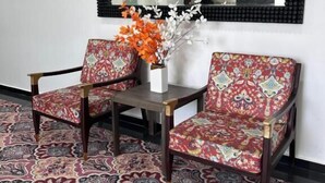A room with two patterned armchairs, a small table, and a mirror with a black frame. - Hotel Tuli Grand Imperial (Nagpur)