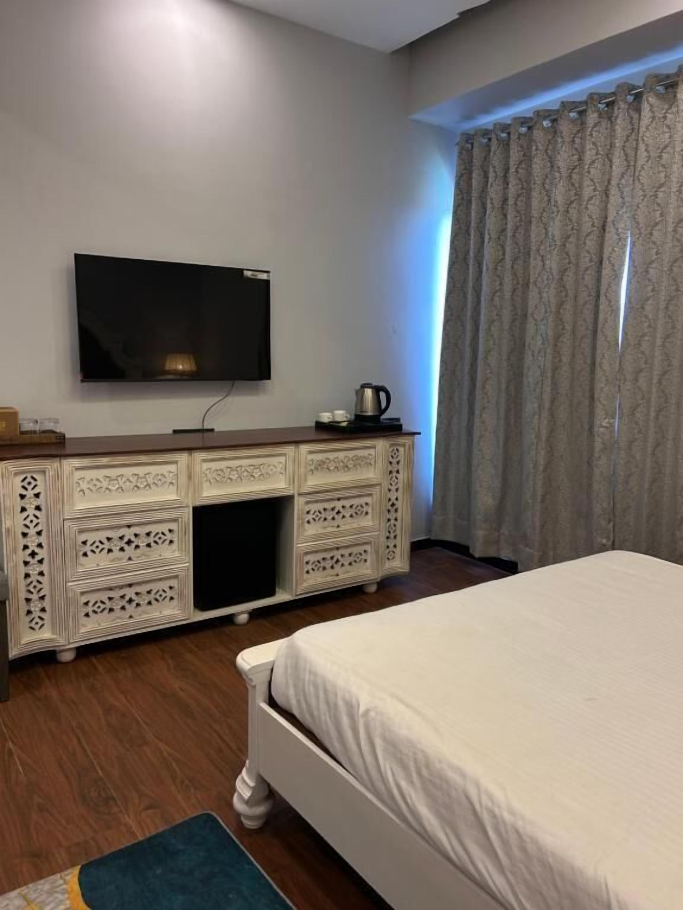 A bedroom with a bed, a TV, a dresser, and a window with curtains.