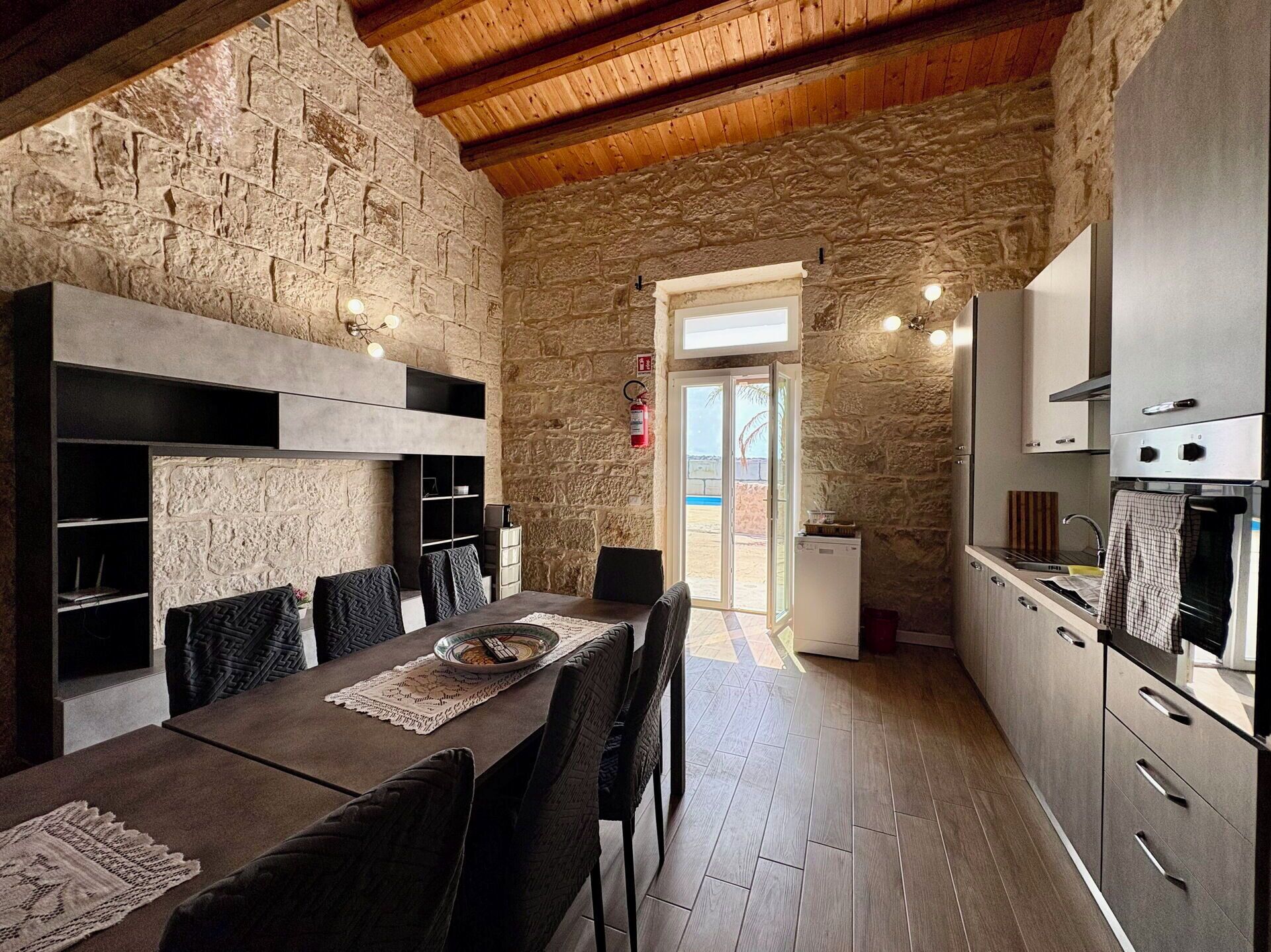 Un espace repas agrémenté d’un mur en pierre, d’un plafond en bois et d’appareils électroménagers modernes.