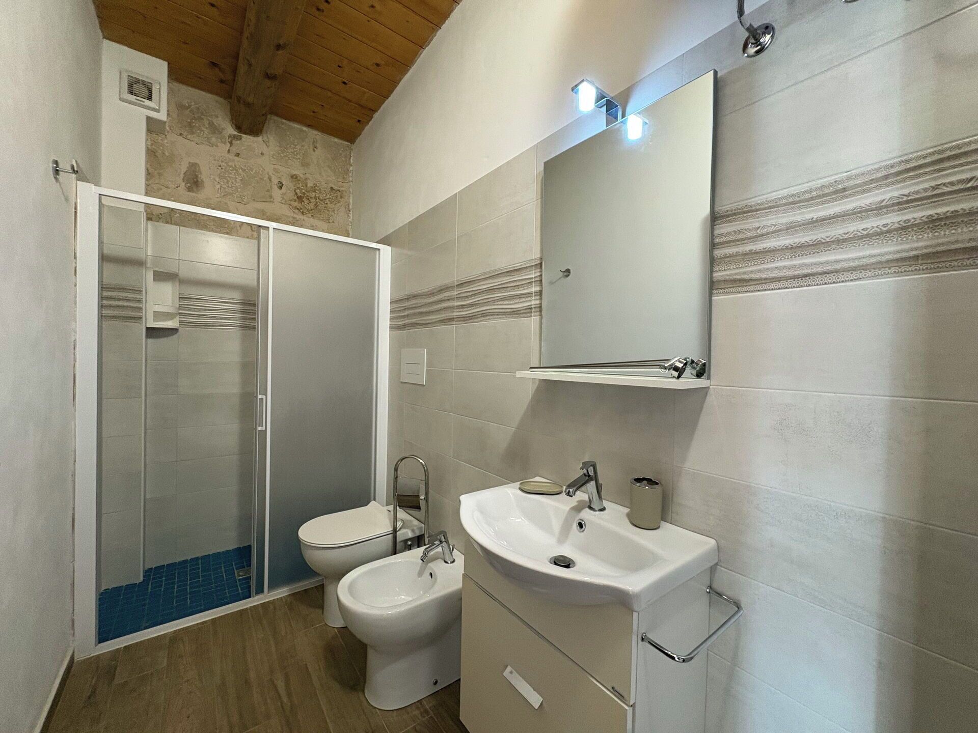 Une salle de bain équipée d’une douche, de toilettes et d’un lavabo, avec un plafond en bois et des murs carrelés.