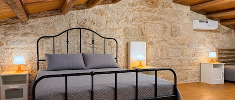 Ein Schlafzimmer mit Steinwand, Holzbalkendecke, Metallbettgestell und Nachttischlampen.