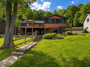 Ein zweistöckiges Holzhaus mit einem Balkon, einer Laube und einer Steintreppe, die zum Eingang führt.