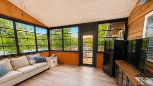 Un intérieur moderne avec un plafond en bois, de grandes fenêtres, un canapé, un téléviseur et un réfrigérateur.