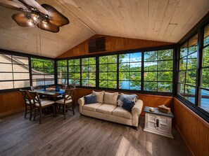 Ein Zimmer mit Holzboden, großen Fenstern, einer Couch, einem Esstisch mit Stühlen und einem Deckenventilator.