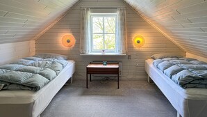 Um quarto de sótão pequeno e acolhedor, com duas camas de solteiro, uma mesinha e uma janela com cortinas.