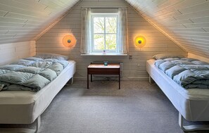A small, cozy attic bedroom with two single beds, a small table, and a window with curtains. - Beautiful home in Thisted with house sea view (Thisted)