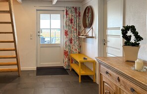 Um quarto com uma escada de madeira, uma porta com janela, uma pequena mesa de madeira, um espelho, uma planta em vaso e um aparador.