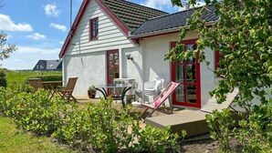 Uma casa com telhado inclinado, porta vermelha e um pequeno pátio com móveis de exterior.