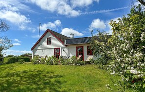 A white house with red trim and a sloped roof, surrounded by green grass and flowering trees. - Beautiful home in Thisted with house sea view (Thisted)
