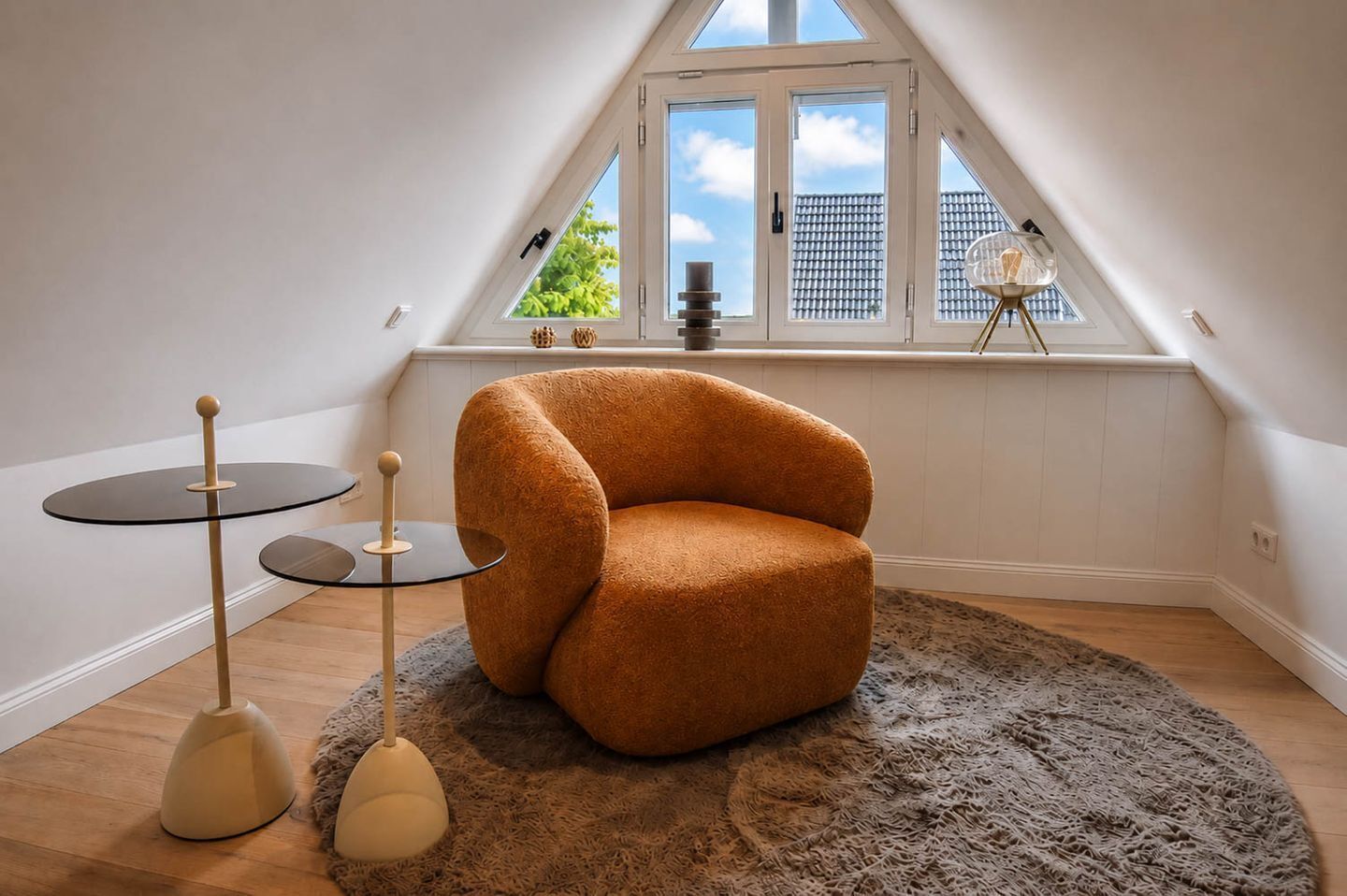 A cozy room with a sloped ceiling, a round orange chair, a small round table, and a floor lamp.