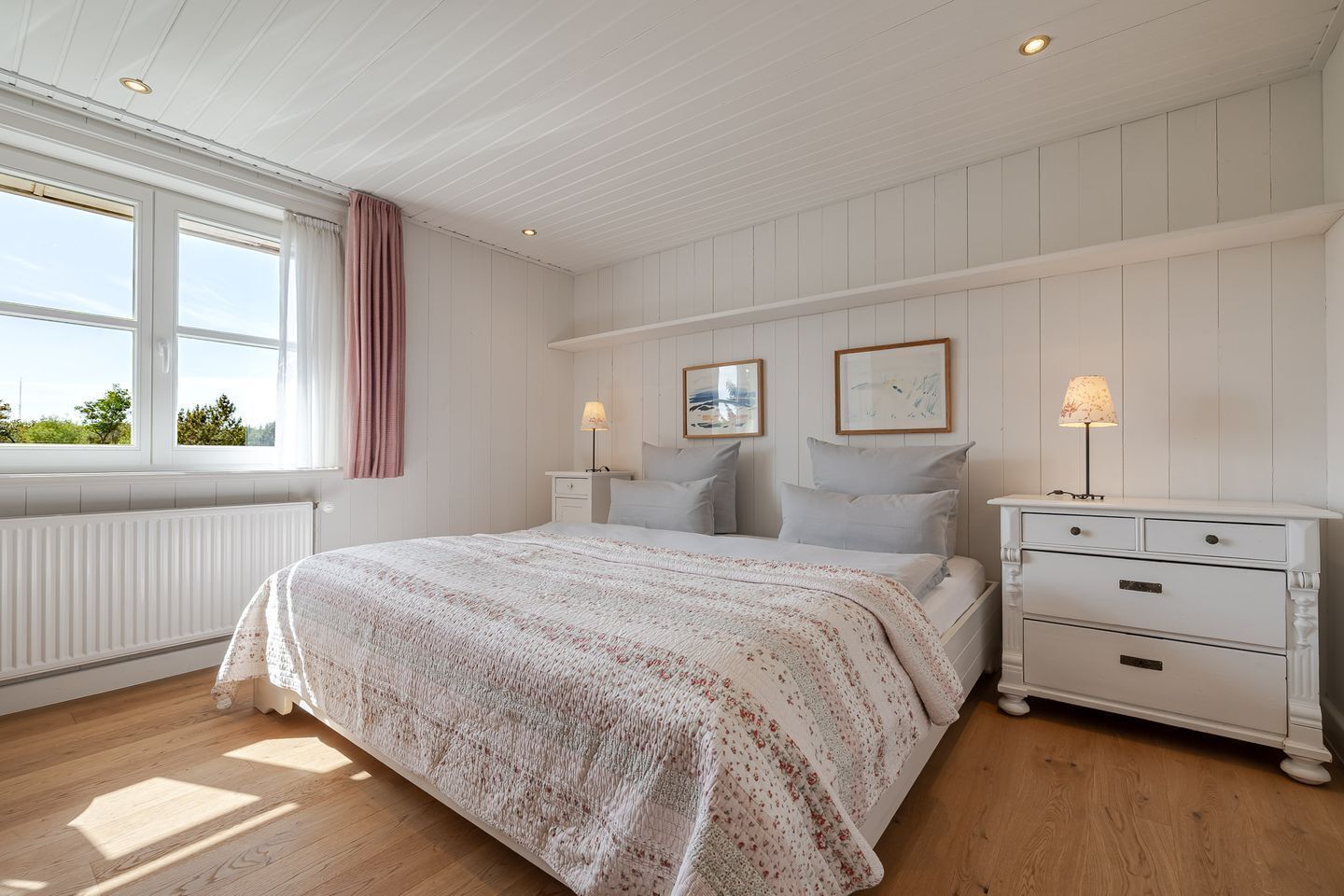 Un dormitorio con cama, mesitas de noche, cómoda y ventana con cortinas.