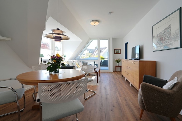 A modern living room with a dining area, wooden flooring, and a large window offering a view. - House Wendt Apartment 01 - House Wendt (Ratekau)