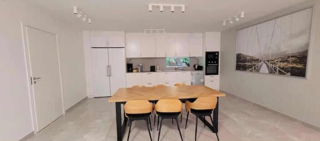 A modern kitchen with white cabinets, a wooden dining table with four chairs, and a large painting on the wall.