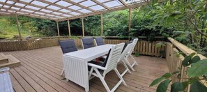 Eine überdachte Terrasse mit Tisch und Stühlen, umgeben von einer Holzterrasse und einem Holzzaun.