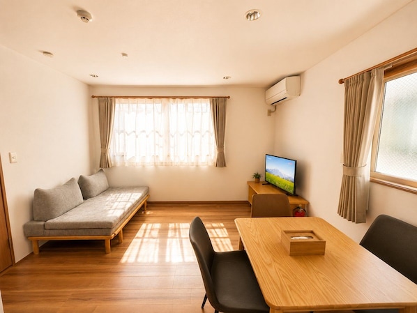 A compact living space with a sofa, a dining table, a television, and a window with curtains.