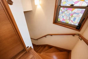 A wooden staircase with a handrail, a stained glass window above, and a door on the left.