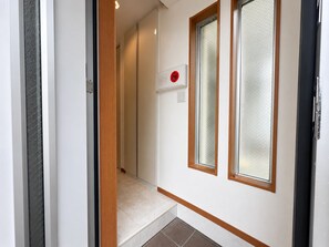 A hallway with a wooden door frame, a white wall, and a red emergency alarm.