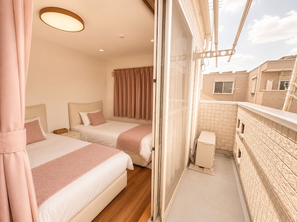 A hotel room with two beds, a balcony, and a view of the cityscape.