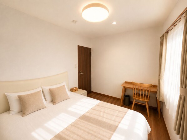A hotel room with a bed, a wooden desk, a chair, and a door.